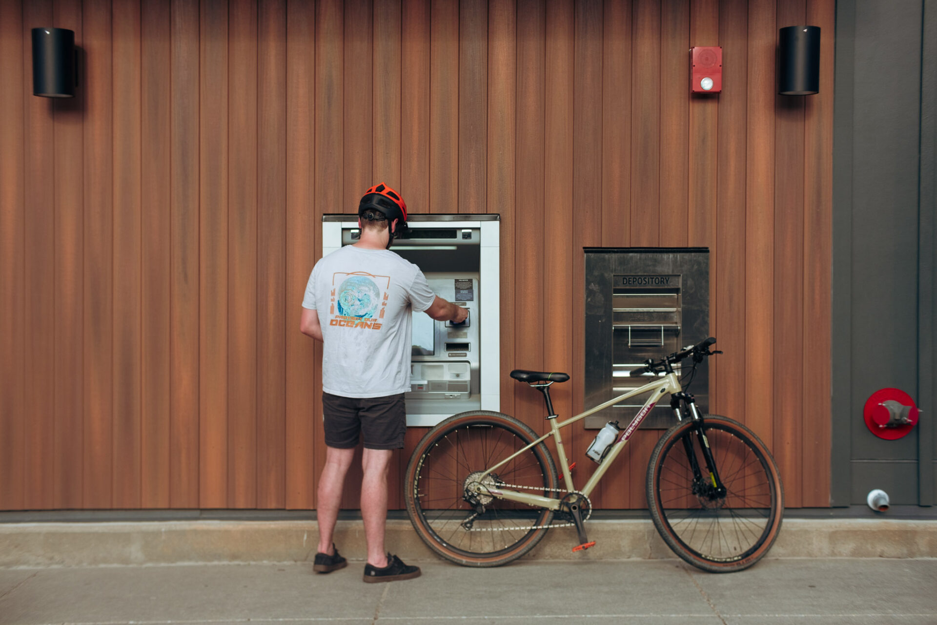 A man, riding a bike, uses an ATM in a bank drive-thru.