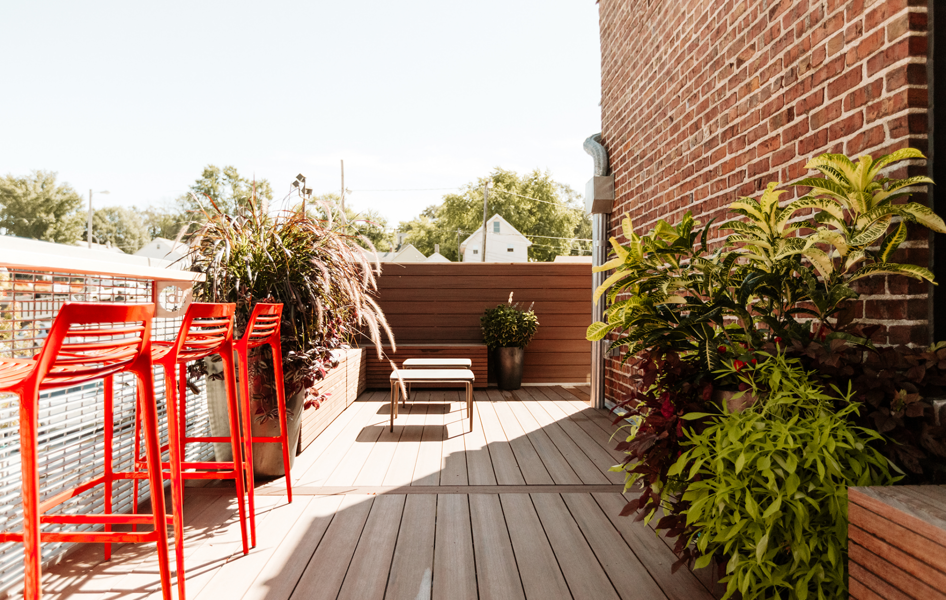 A rooftop deck with red stools, plants, and a coffee table.