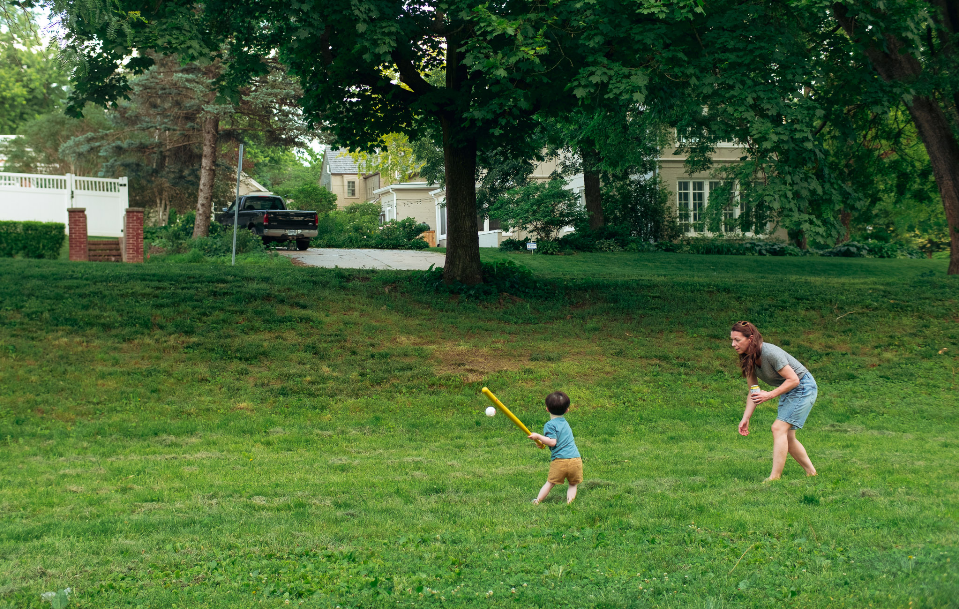 A mom and son play baseball in a park.