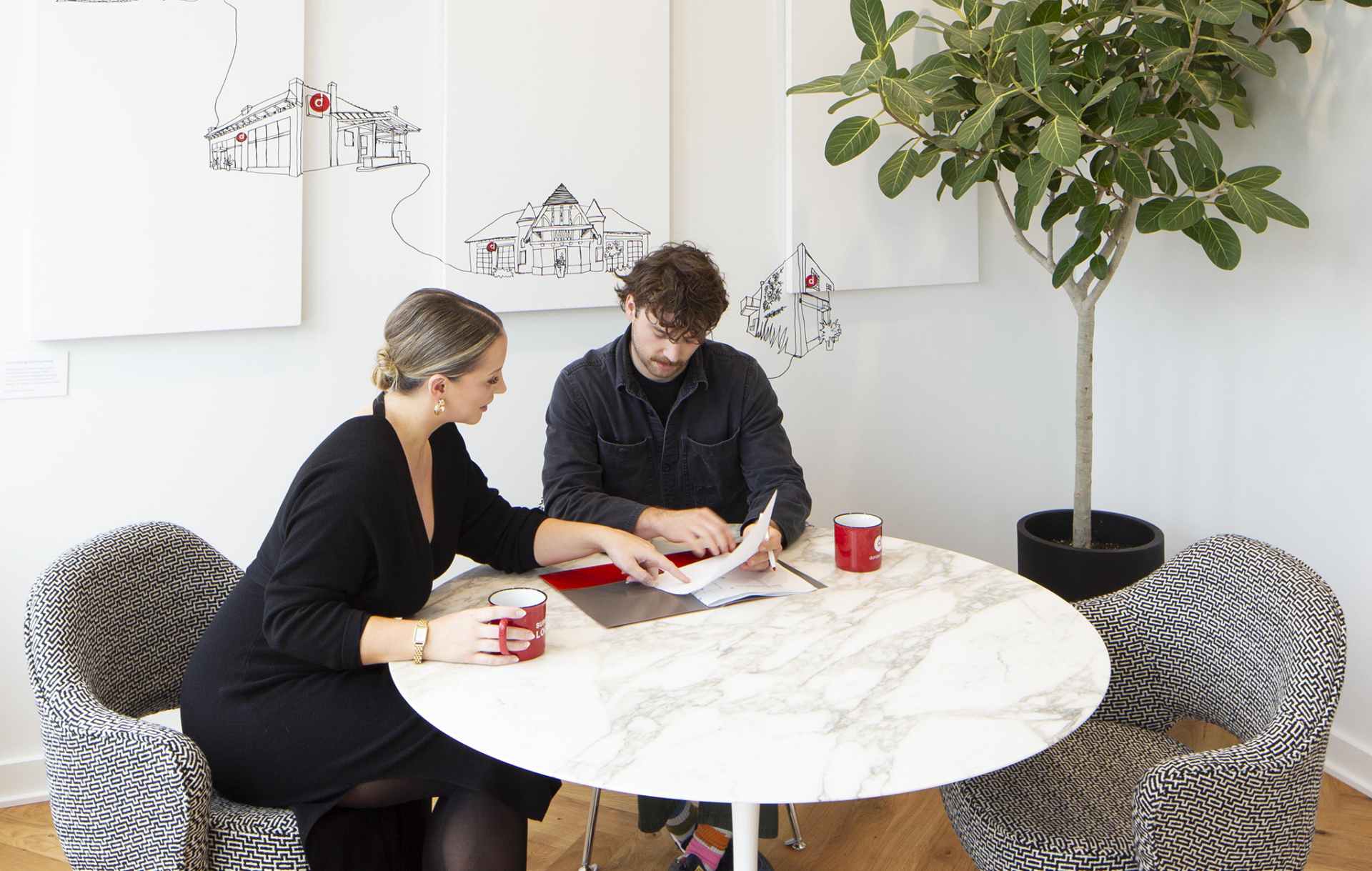 A man and a woman sit at a white table looking over paperwork.