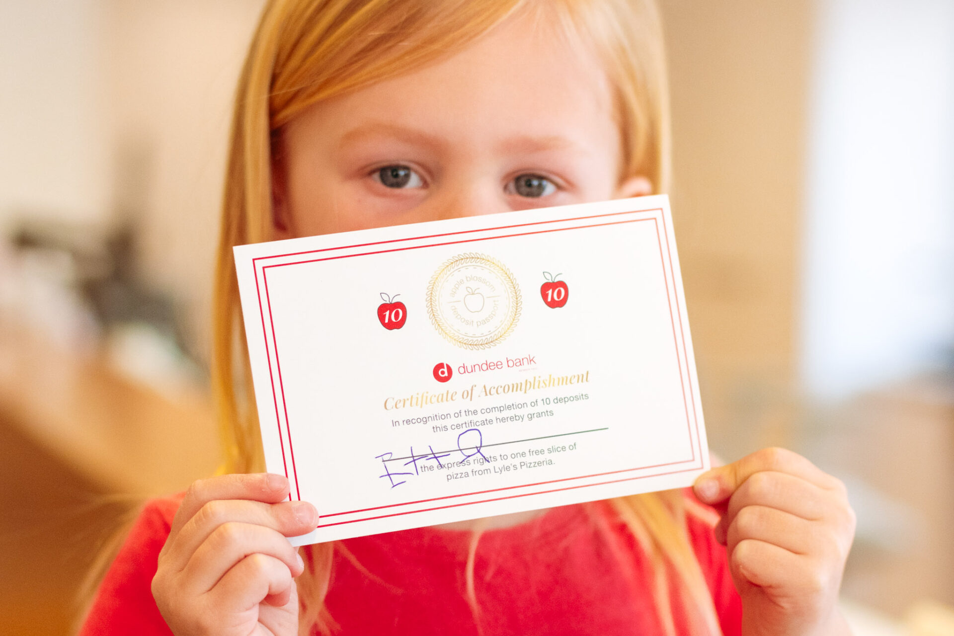 A child in a red shirt holding up a piece of paper in front of her face.