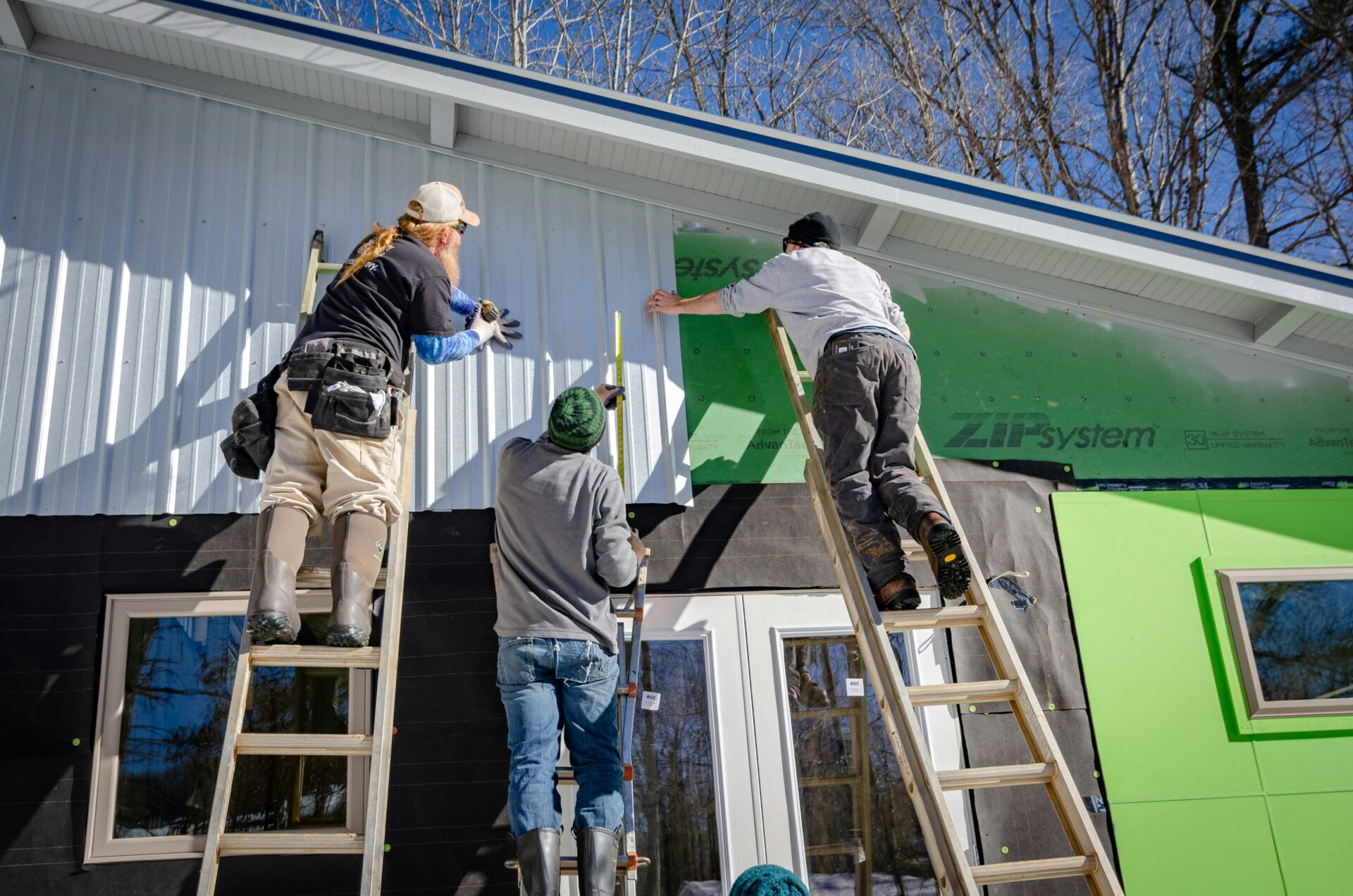 Three men install siding on a house.