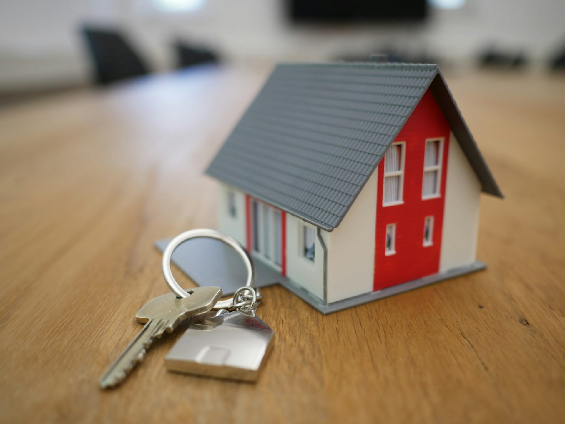 A keychain sits on a table next to a small model house.
