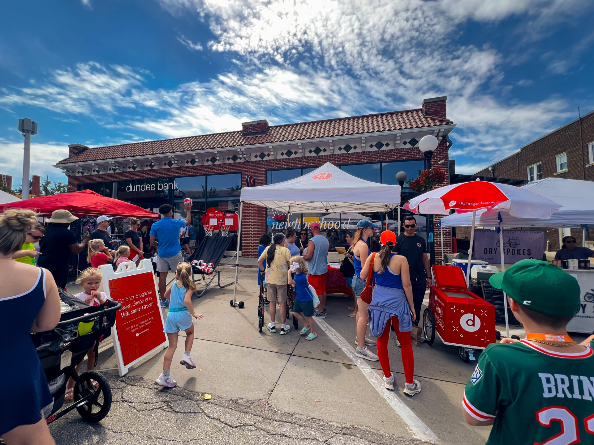 A crowd of people at a street fair stand in the line to get popsicles from a vendor tent.
